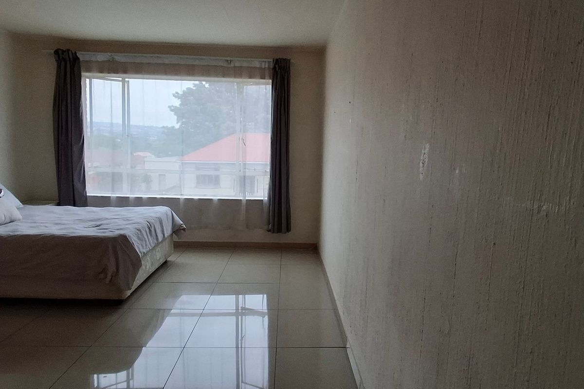 A bedroom featuring tiled flooring and a large window, providing natural light and a view of the surrounding area.