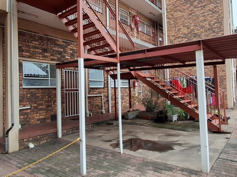 Exterior view of an apartment complex featuring a brick facade, external metal staircase, and paved communal courtyard area with covered parking.