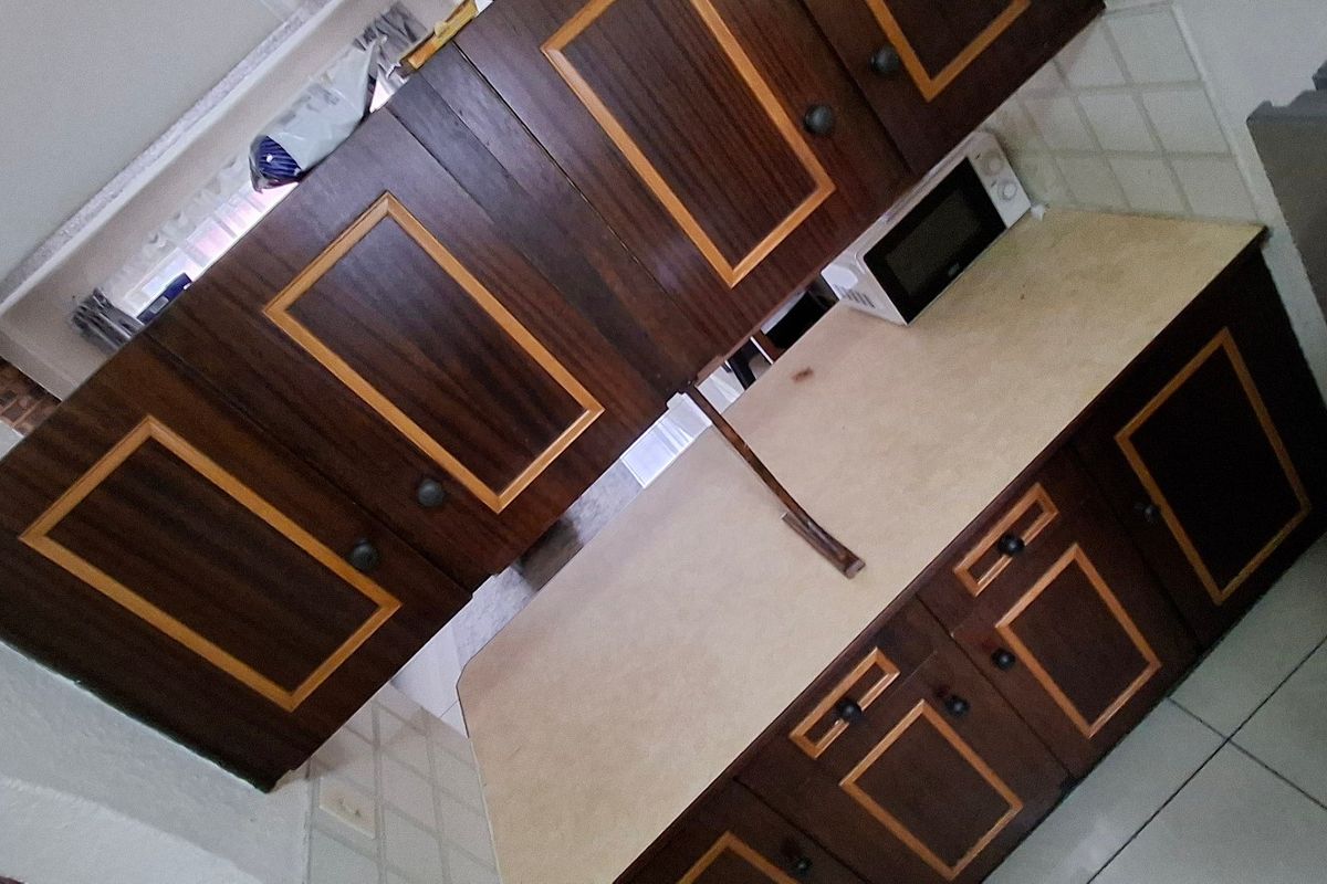 A dated kitchen featuring dark wood-toned cabinetry with contrasting trim, laminate countertops, and tiled backsplash, offering potential for a modern renovation.