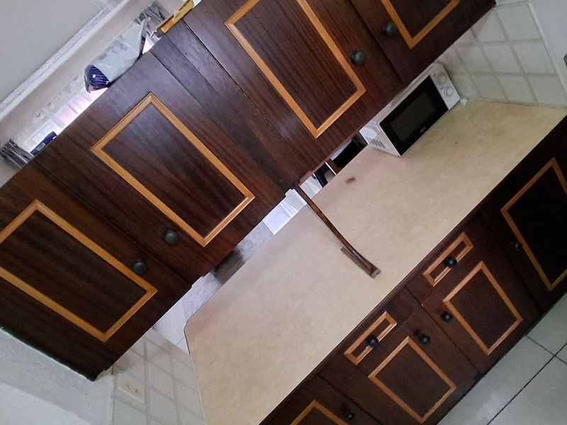 A dated kitchen featuring dark wood-toned cabinetry with contrasting trim, laminate countertops, and tiled backsplash, offering potential for a modern renovation.