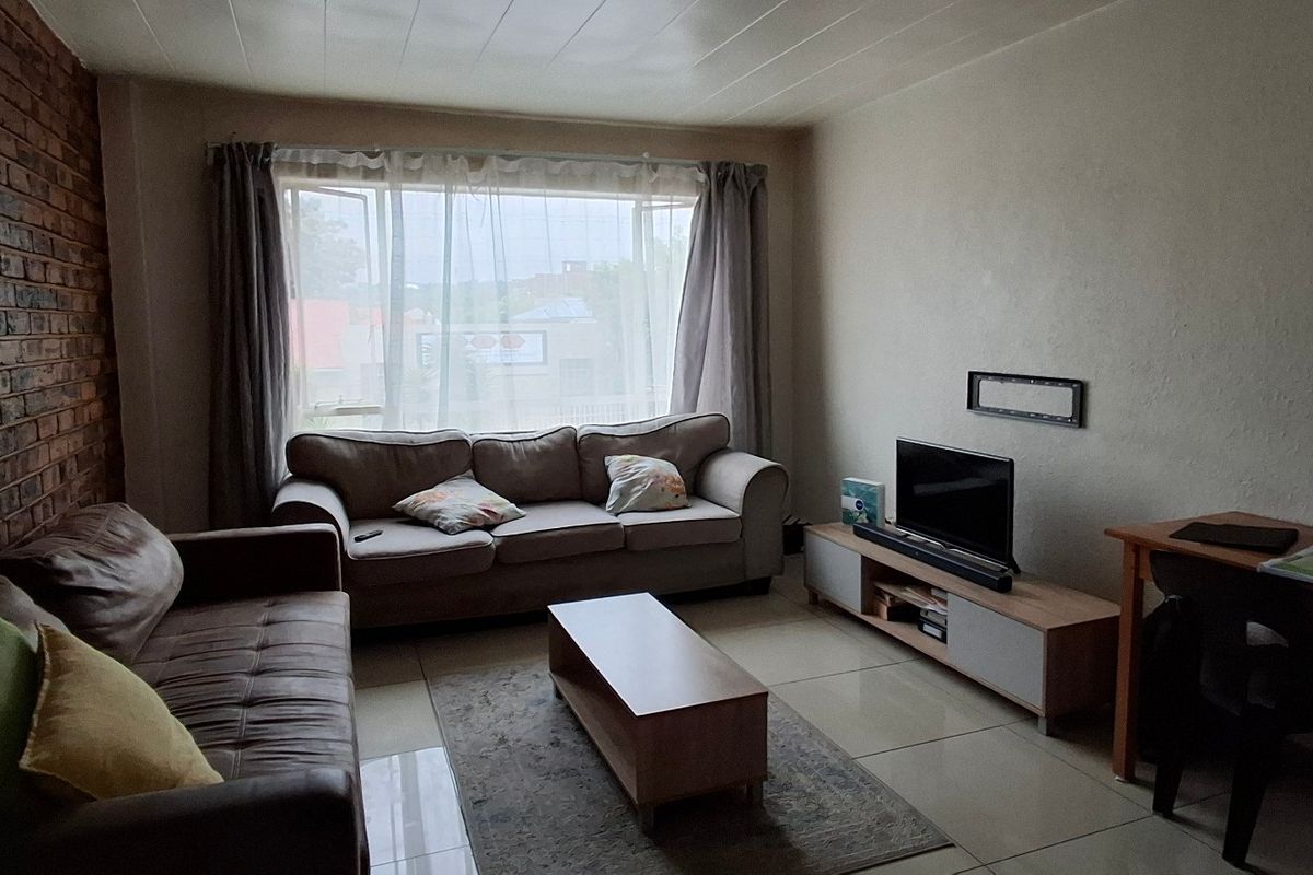A living room featuring an exposed brick feature wall, tiled flooring, and a large window allowing natural light into the space.