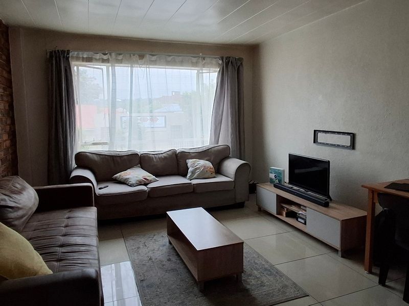 A living room featuring an exposed brick feature wall, tiled flooring, and a large window allowing natural light into the space.