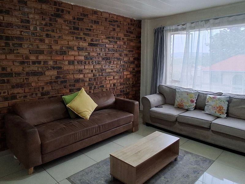 A living room featuring a prominent exposed brick feature wall, large window for natural light, and neutral tiled flooring.