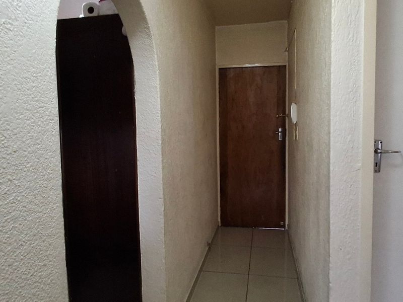 A narrow interior hallway featuring tiled flooring and an arched entryway, connecting multiple rooms within the apartment.