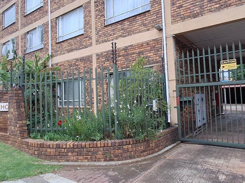 Exterior view of the apartment complex entrance featuring face brick facade, secure steel fencing with electric security, and a gated driveway access point.