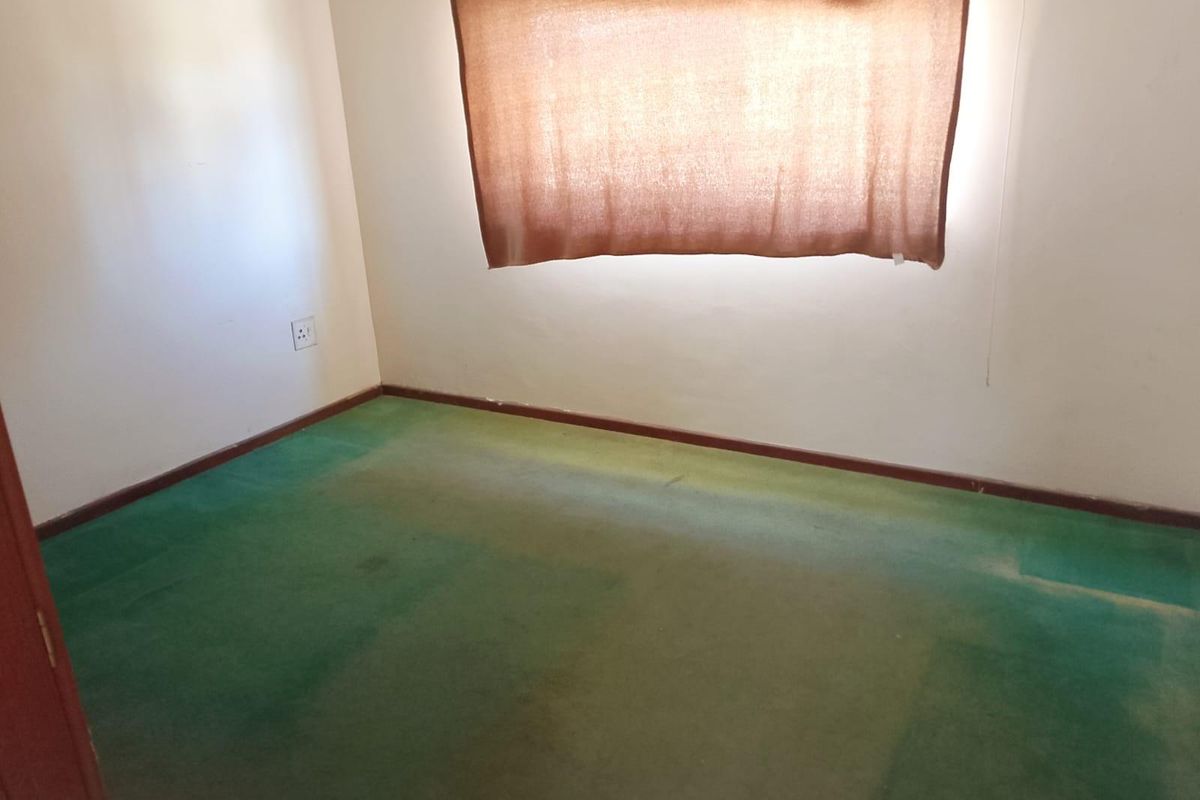 An empty bedroom featuring worn green carpeting and neutral walls, providing a blank canvas for renovation or interior design updates.