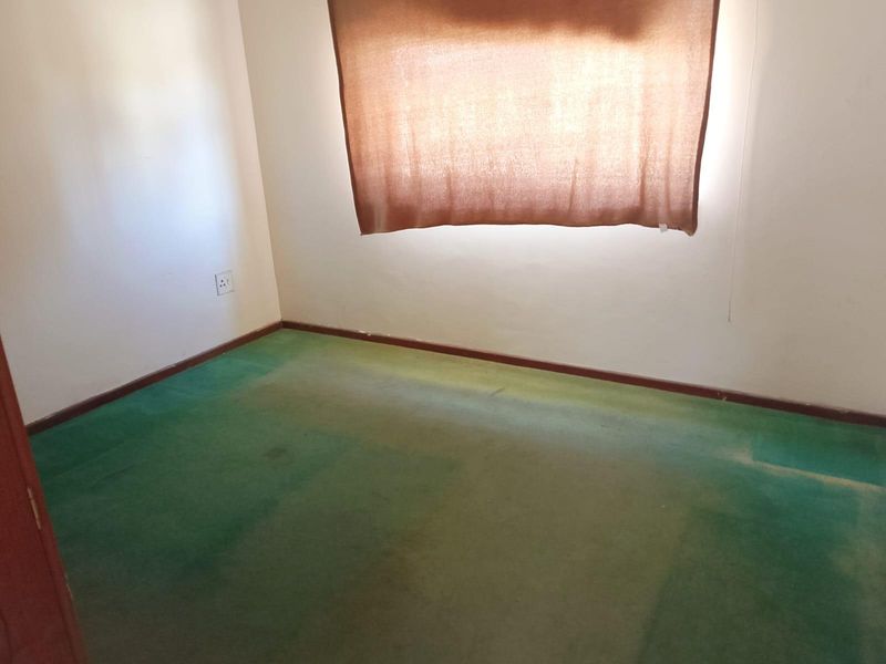 An empty bedroom featuring worn green carpeting and neutral walls, providing a blank canvas for renovation or interior design updates.