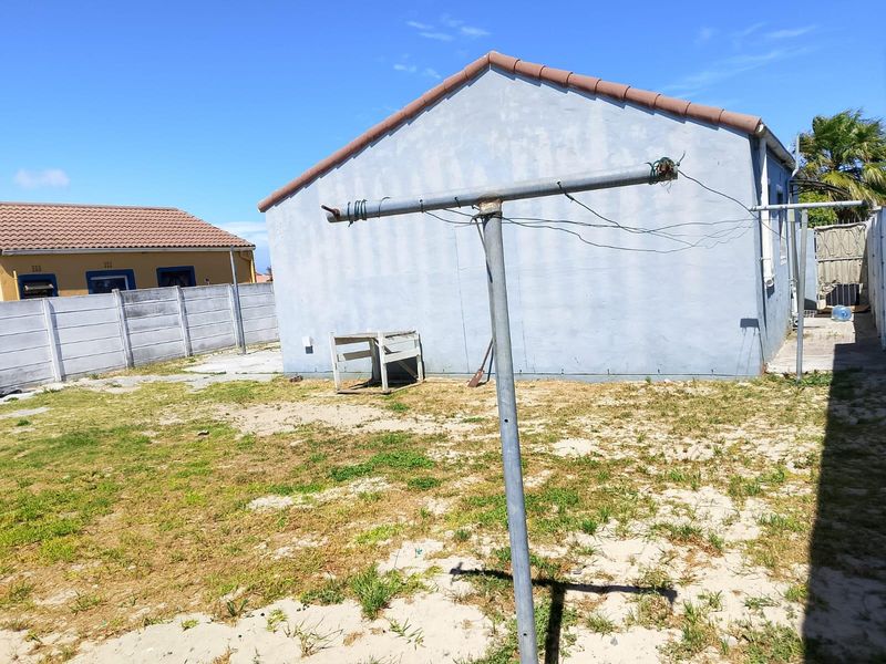 Rear exterior view of the property featuring a tiled roof, precast concrete boundary wall, and a large backyard area with a metal washing line.
