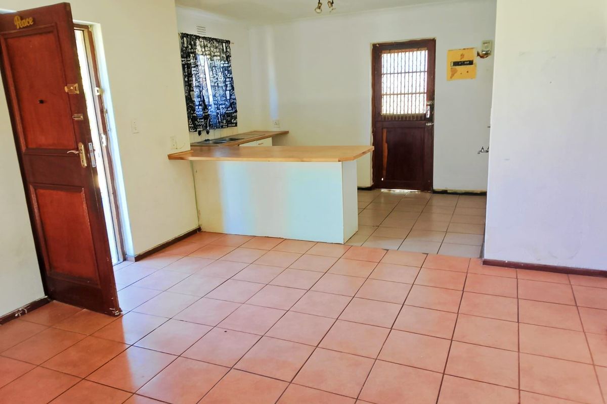 An open-plan living and kitchen area featuring tiled flooring, a breakfast bar, and direct access to exterior doors.