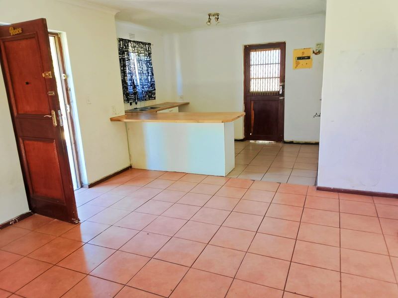 An open-plan living and kitchen area featuring tiled flooring, a breakfast bar, and direct access to exterior doors.