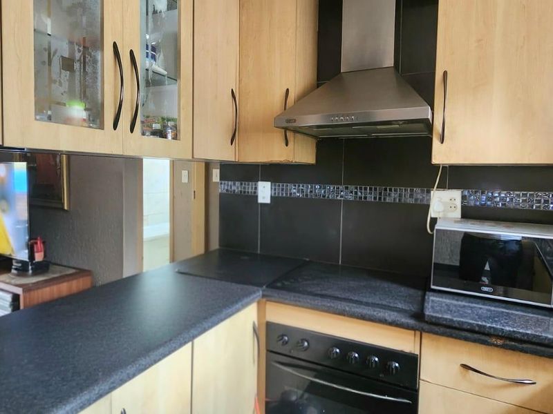 A functional kitchen featuring light wood cabinetry, dark granite countertops, a built-in oven, and a stainless steel extractor fan with a tiled backsplash.