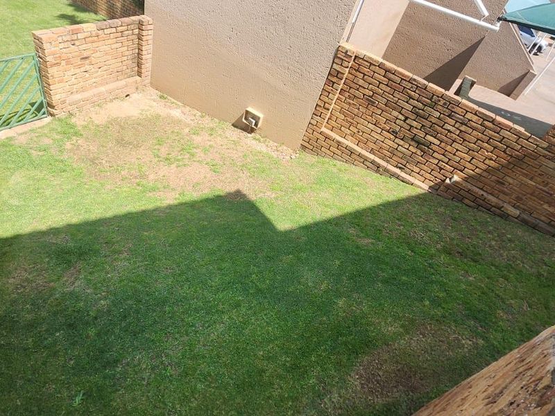 A private rear garden area featuring brick boundary walls, a small metal gate, and a grass lawn.