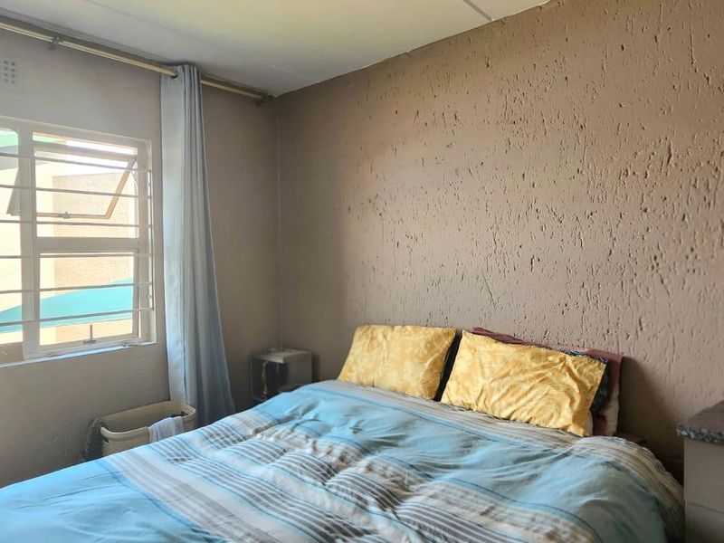 A bedroom featuring textured walls and a window fitted with security bars, providing natural light and ventilation.