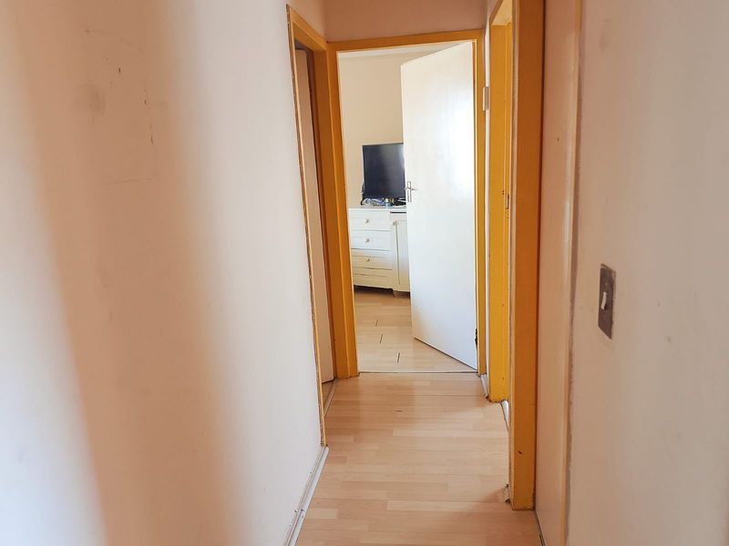 A narrow interior hallway featuring laminate flooring and yellow-painted door frames, leading into an adjacent bedroom space.
