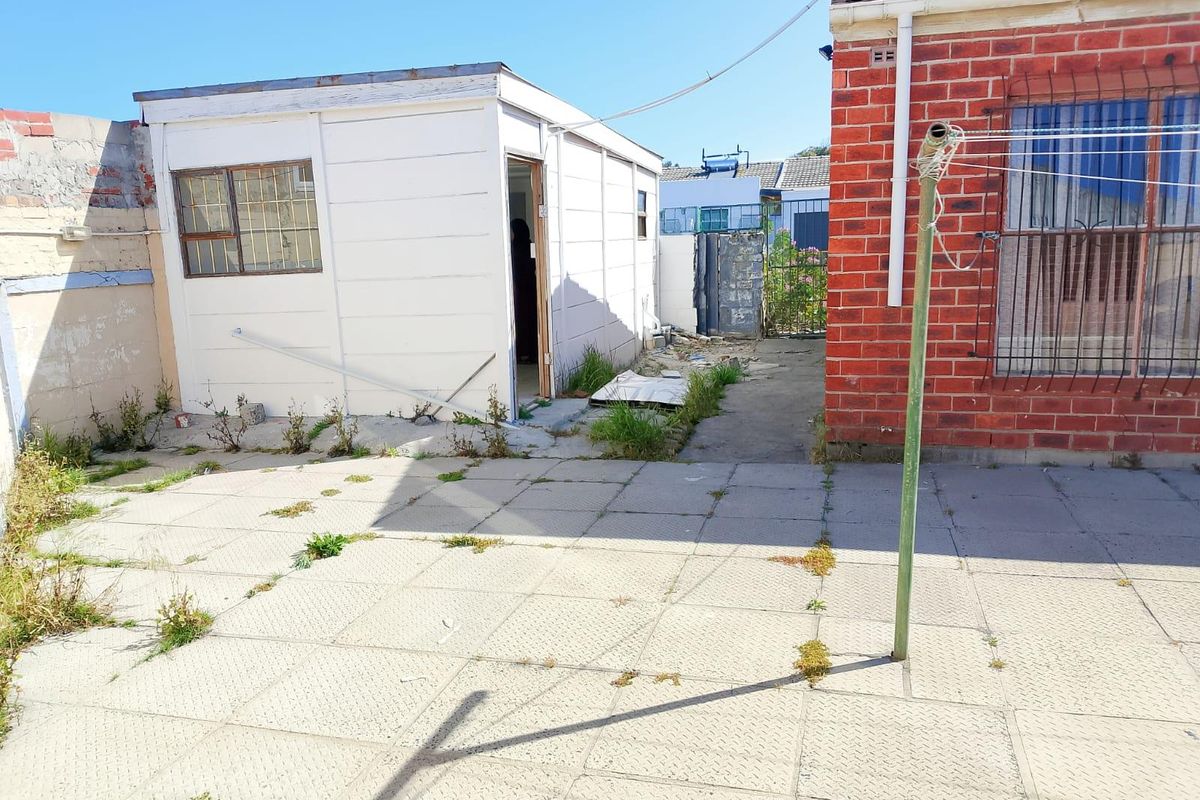 Rear exterior view showing a paved courtyard area, a brick main building facade, and a detached outbuilding structure.