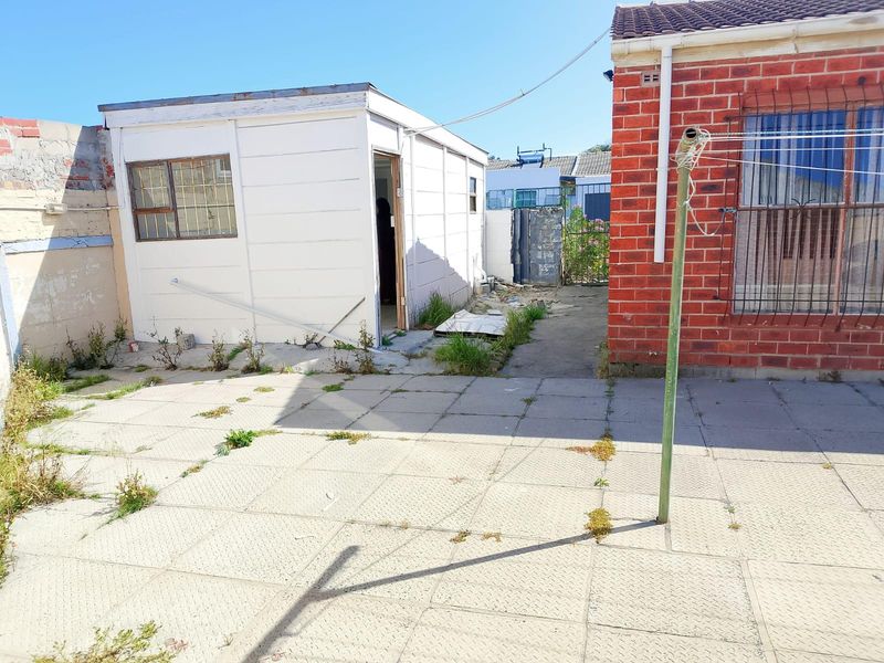 Rear exterior view showing a paved courtyard area, a brick main building facade, and a detached outbuilding structure.
