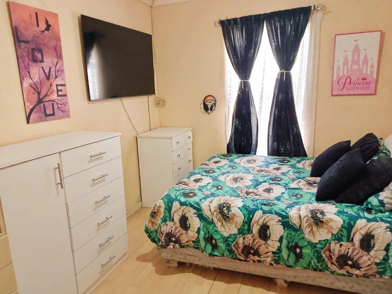 A bedroom featuring laminate flooring and a window with curtains. The room requires cosmetic updates including fresh paint to improve its overall condition.
