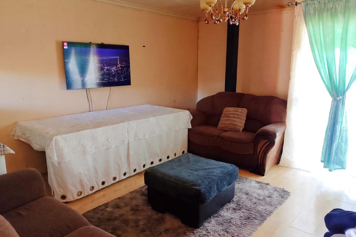 A living room featuring laminate flooring and a central chandelier, requiring cosmetic updates to the wall finishes to improve the overall aesthetic.