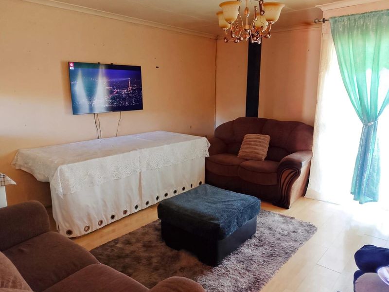 A living room featuring laminate flooring and a central chandelier, requiring cosmetic updates to the wall finishes to improve the overall aesthetic.