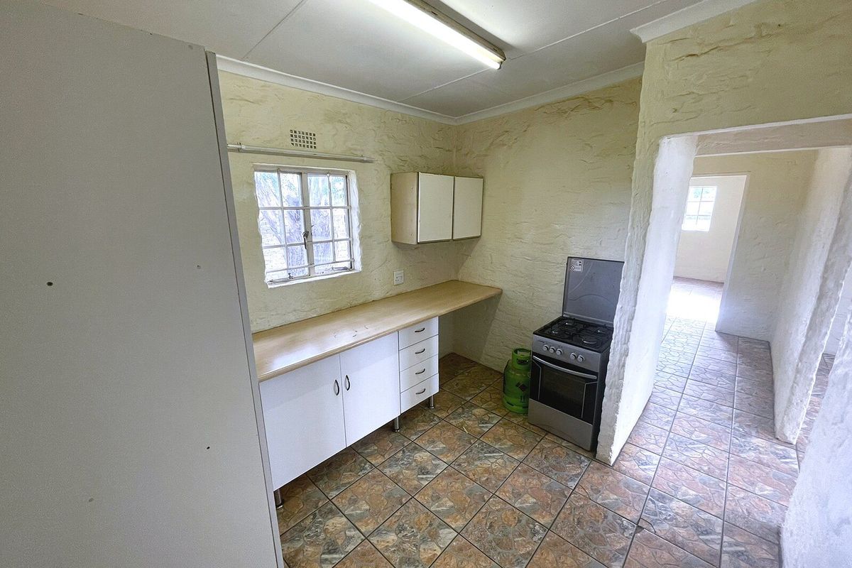 A functional kitchen area featuring tiled flooring, built-in cabinetry with laminate countertops, and a gas stove, offering a blank canvas for renovation.