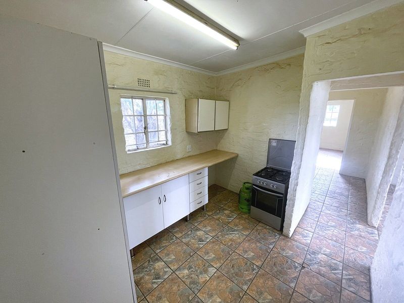 A functional kitchen area featuring tiled flooring, built-in cabinetry with laminate countertops, and a gas stove, offering a blank canvas for renovation.