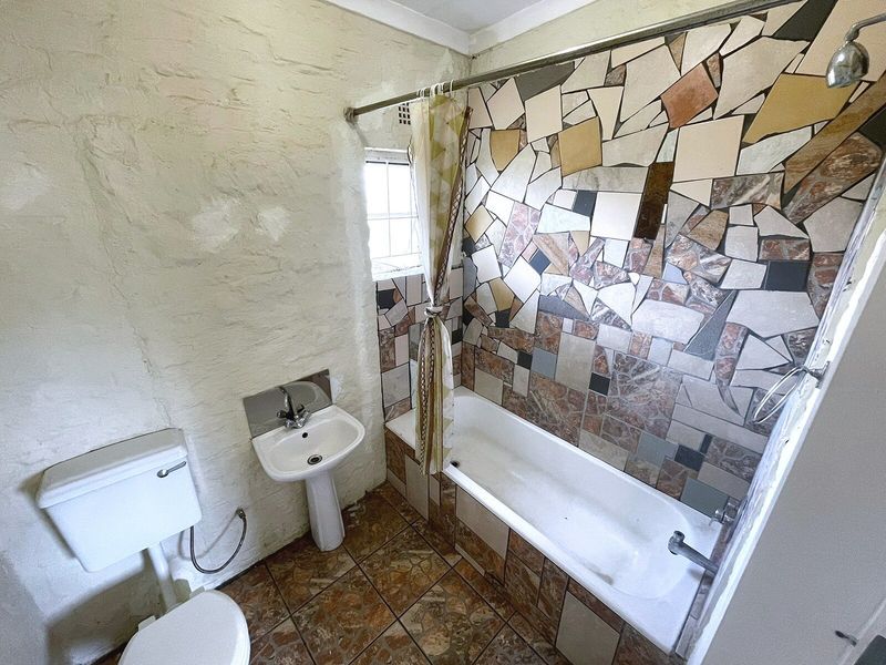 A functional bathroom featuring a pedestal basin, toilet, and a bathtub with a unique mosaic tile surround and tiled flooring.