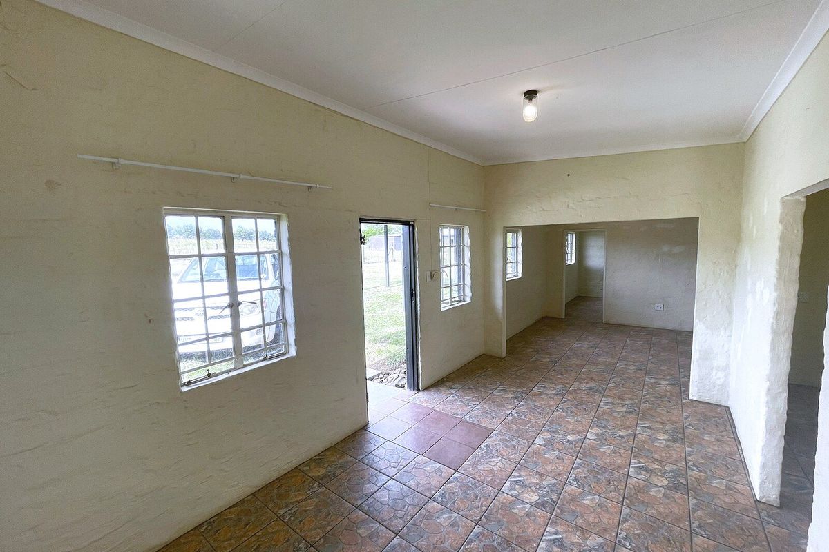 An empty, open-plan living area featuring tiled flooring, textured walls, and multiple steel-framed windows providing natural light.