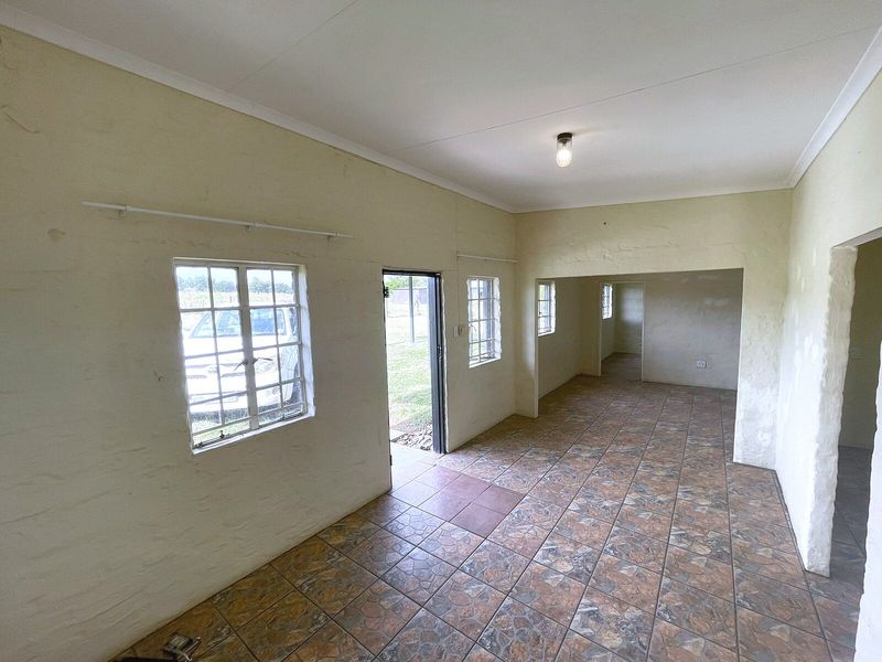 An empty, open-plan living area featuring tiled flooring, textured walls, and multiple steel-framed windows providing natural light.