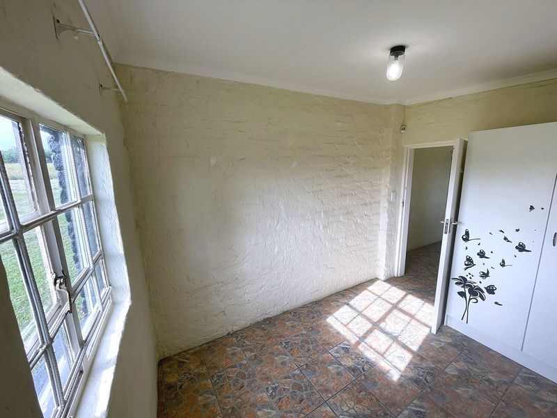 A vacant bedroom featuring painted brick walls, tiled flooring, and a built-in cupboard, offering a blank canvas for renovation.