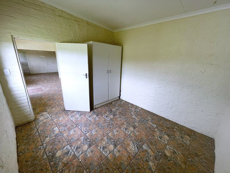 A vacant bedroom featuring tiled flooring, painted brick walls, and a built-in wardrobe, offering a blank canvas for renovation.