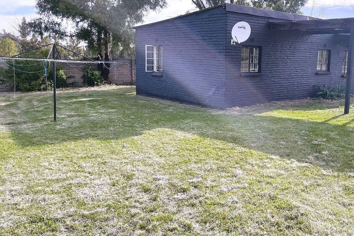 Rear view of the property featuring a painted brick exterior, steel-framed windows, and a spacious garden area with a boundary wall.