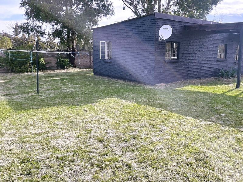 Rear view of the property featuring a painted brick exterior, steel-framed windows, and a spacious garden area with a boundary wall.