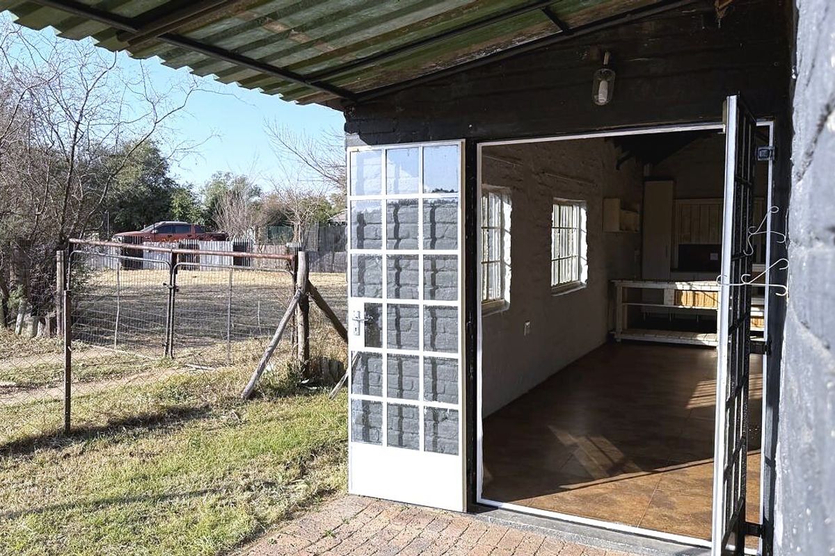 A covered patio area featuring brick paving and french doors leading into the interior space, with a corrugated metal roof overhead.