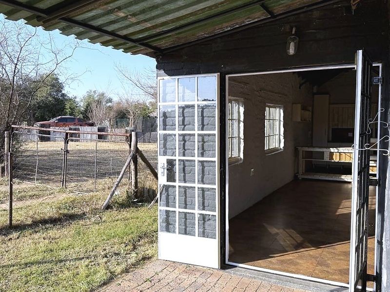 A covered patio area featuring brick paving and french doors leading into the interior space, with a corrugated metal roof overhead.