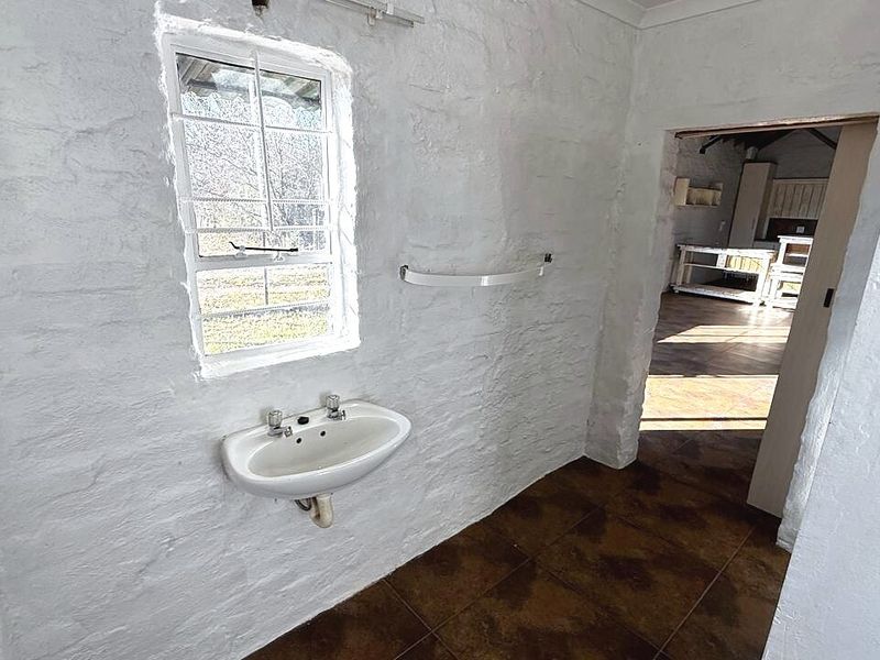 A small, empty bathroom featuring white textured walls, tiled flooring, and a wall-mounted basin with security bars on the window.