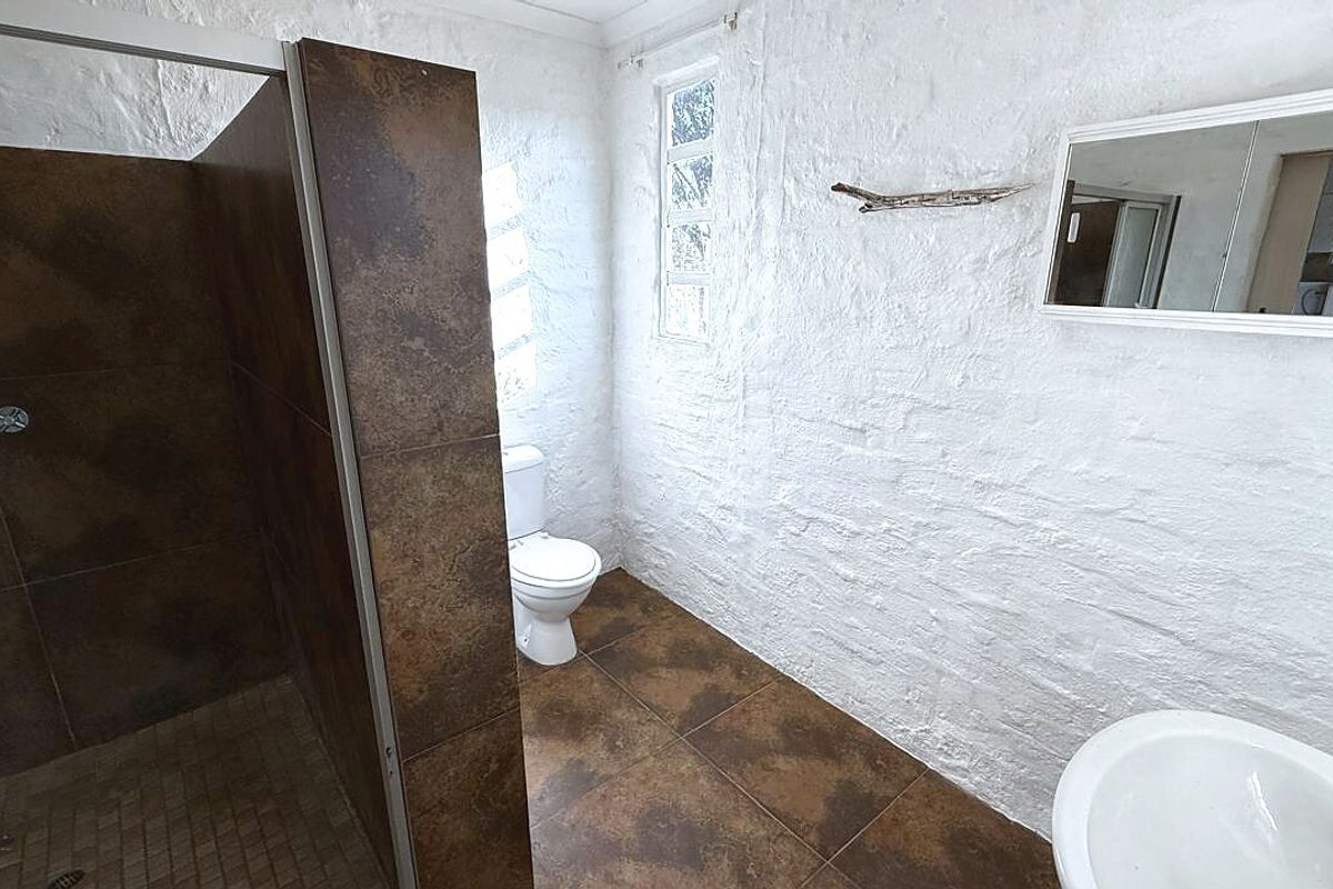 A functional bathroom featuring a walk-in shower with dark tiling, a pedestal basin, and a toilet, finished with textured white walls.