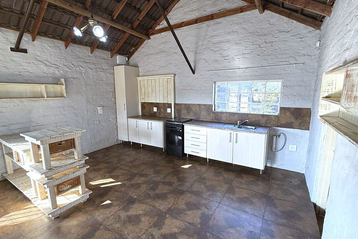 Rustic kitchen featuring exposed timber roof trusses, textured brick walls, tiled flooring, and functional built-in cabinetry with a stainless steel sink.