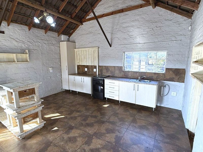 Rustic kitchen featuring exposed timber roof trusses, textured brick walls, tiled flooring, and functional built-in cabinetry with a stainless steel sink.