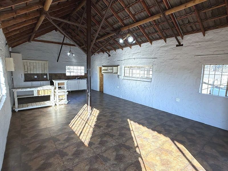 Spacious open-plan living area featuring vaulted ceilings with exposed timber trusses, tiled flooring, and a functional kitchen space with built-in cabinetry.