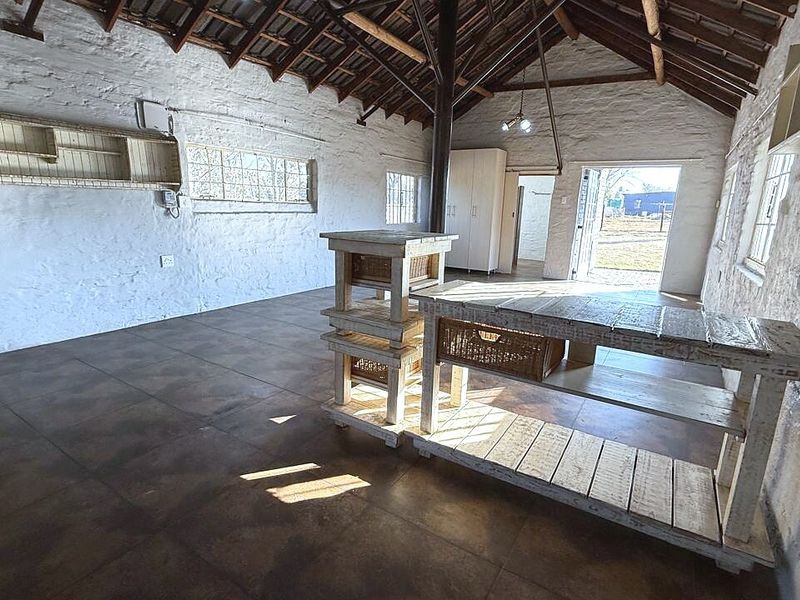A rustic utility space featuring exposed timber roof trusses, painted brick walls, and tiled flooring, offering a versatile area with potential for various uses.