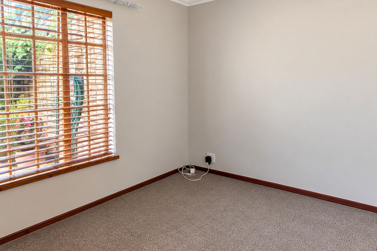 A clean, empty bedroom featuring neutral walls, carpeted flooring, and a large window with wooden blinds overlooking the exterior.