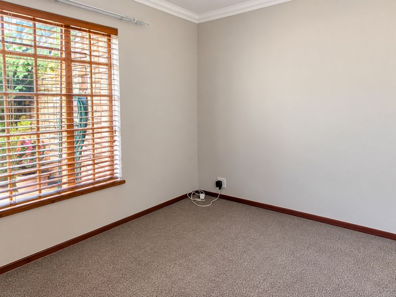 A clean, empty bedroom featuring neutral walls, carpeted flooring, and a large window with wooden blinds overlooking the exterior.