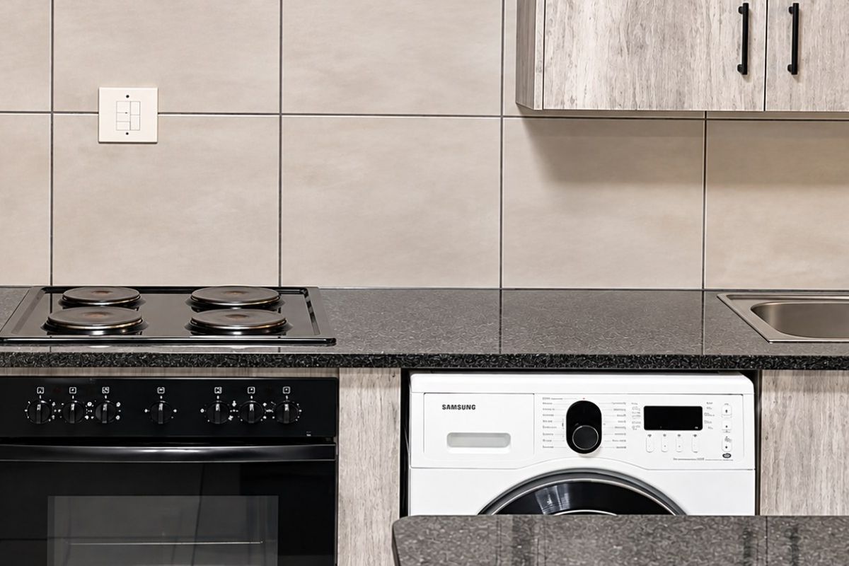 Modern kitchen featuring granite countertops, built-in oven, electric hob, stainless steel double sink, and integrated washing machine with contemporary laminate cabinetry.