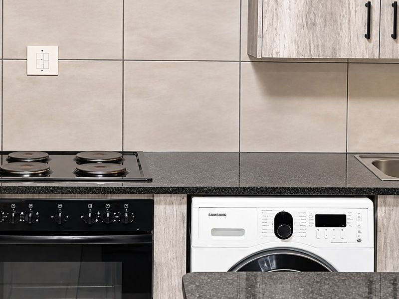 Modern kitchen featuring granite countertops, built-in oven, electric hob, stainless steel double sink, and integrated washing machine with contemporary laminate cabinetry.