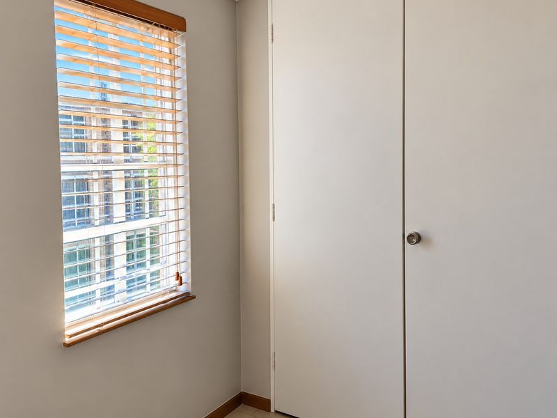 A bright, empty bedroom featuring a built-in wardrobe and timber venetian blinds, offering a clean and neutral space ready for personalization.