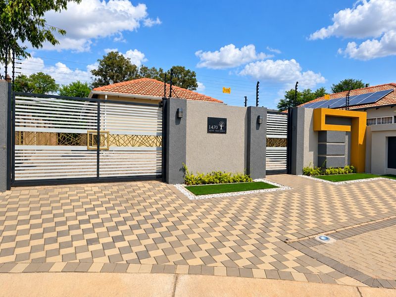 Modern front facade featuring a paved driveway, secure sliding gates, boundary wall with integrated lighting, electric fencing, and roof-mounted solar panels.