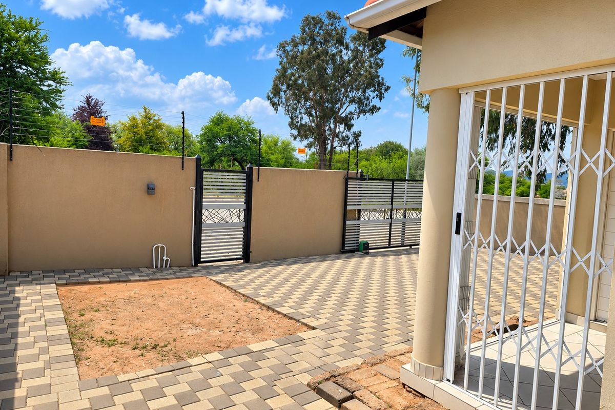 A paved rear courtyard featuring a perimeter wall with electric fencing, a security gate, and a covered patio area with a security trellis door.