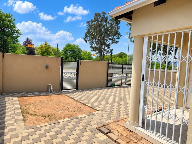 A paved rear courtyard featuring a perimeter wall with electric fencing, a security gate, and a covered patio area with a security trellis door.
