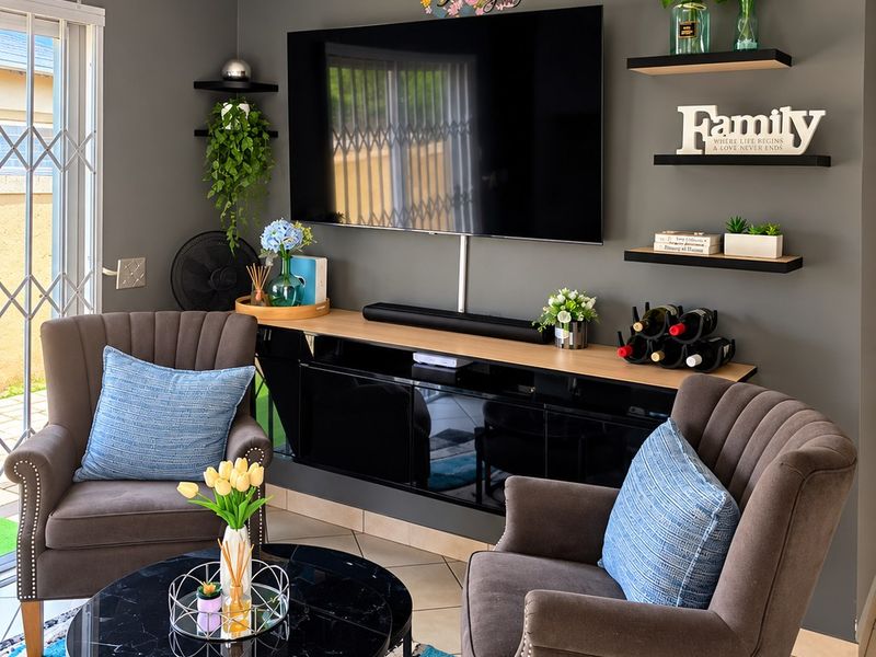 A well-maintained living room featuring tiled flooring, a sliding glass door with security gate, and modern wall-mounted shelving.