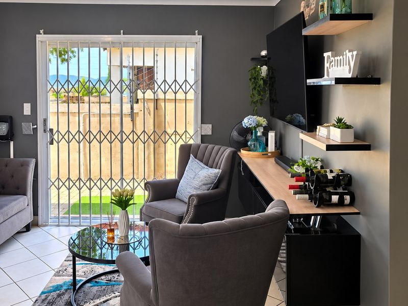 A modern living room featuring tiled flooring, floating wall shelves, and a sliding glass door with a security gate leading to the exterior.